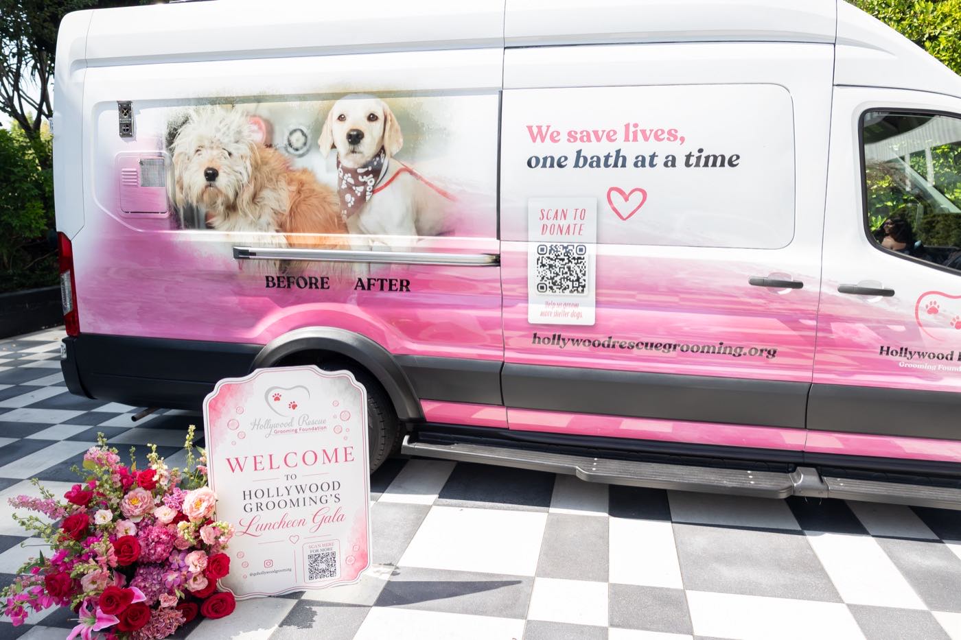 The Hollywood Rescue Grooming Foundation mobile grooming van, painted with a before-and-after of two rescue dogs and the words 'We save lives, one bath at a time', parked beside the welcome sign at the 25th anniversary luncheon gala