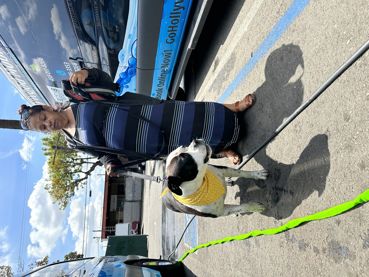 A Skid Row neighbor with her freshly-groomed pit bull mix in a yellow bandana, standing outside the Hollywood Mobile Grooming van during a joint event with Underdog Community Project